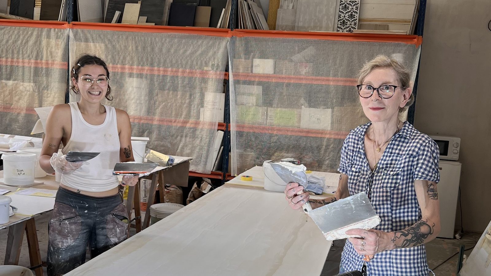 Félicie et Emma souriantes à l'atelier, lisseuses en main, autour d'un grand panneau d'enduit