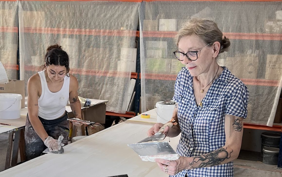 Félicie et Emma lissent ensemble un grand panneau d'enduit à l'atelier