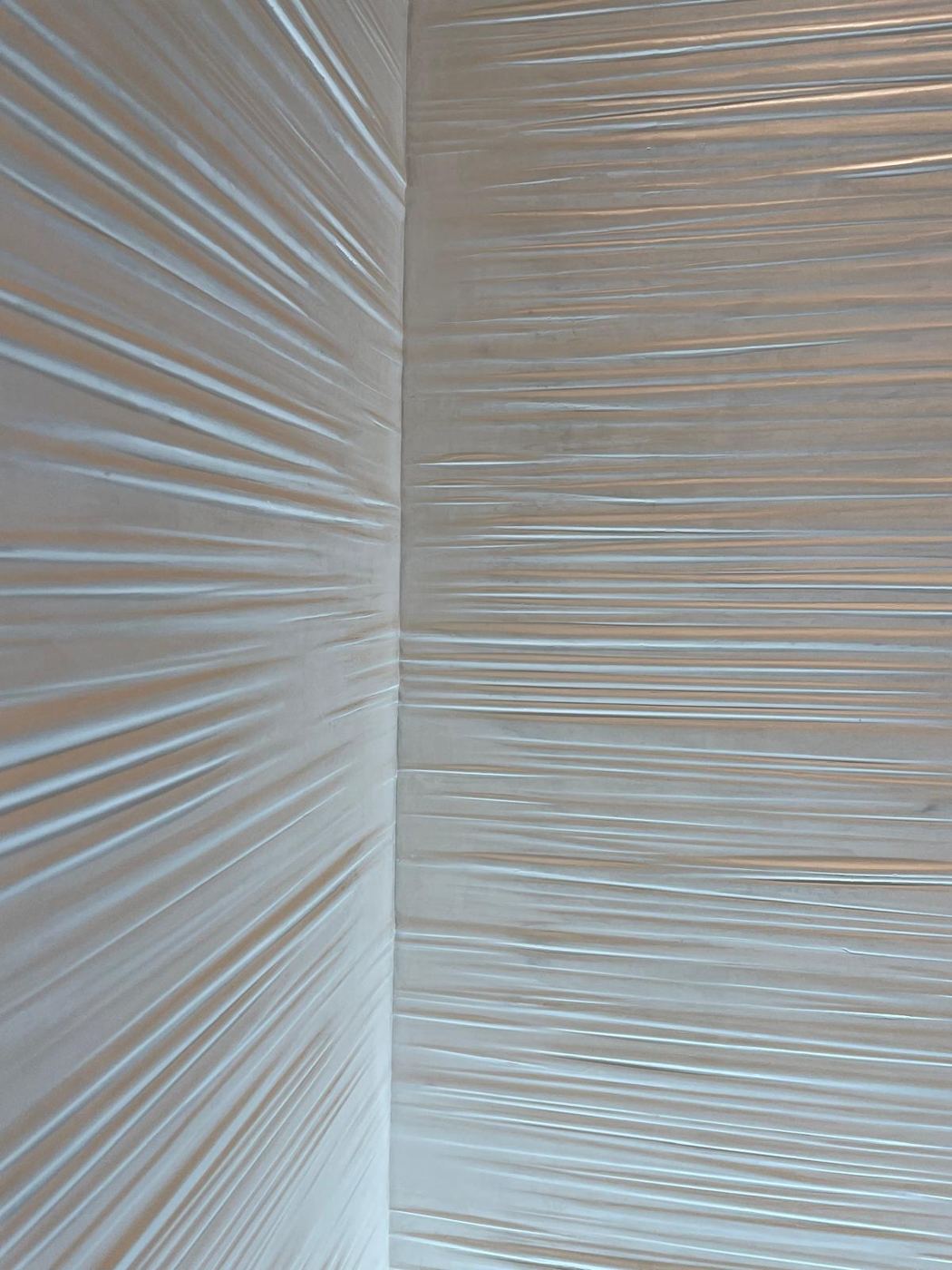 Angle de mur en enduit blanc travaillé en plis horizontaux, comme un drapé