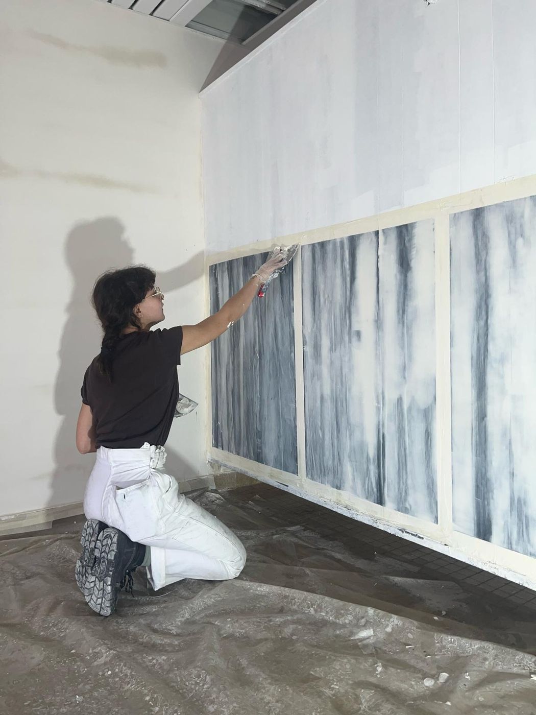 Félicie à genoux pose de l'enduit gras sur une série de panneaux aux veines gris-bleu